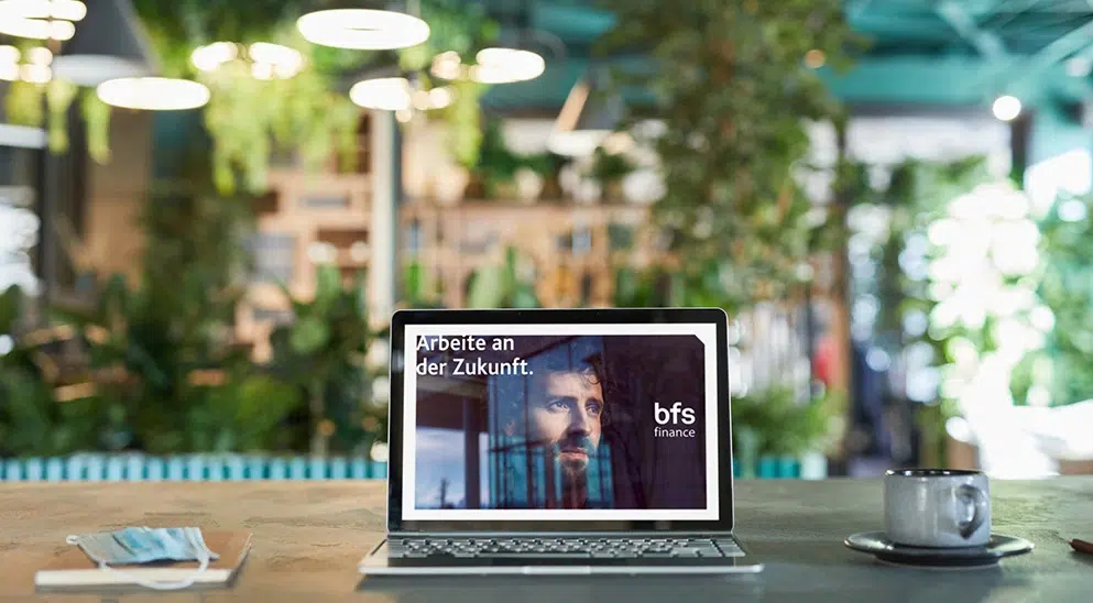 Banner von BFS finance zum Arbeiten an der Zukunft, Laptop auf einem Tisch im freien